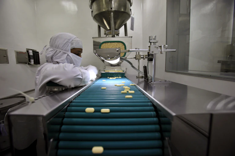 Pharmacist observing pills on a conveyor belt in a lab.