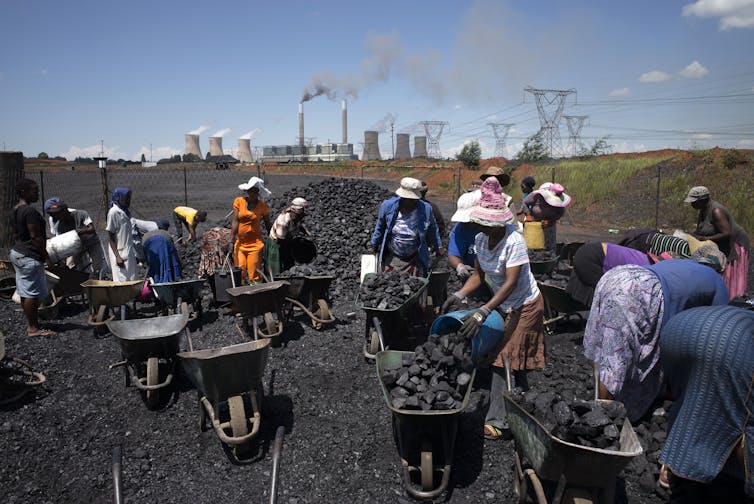 Women load coal from a pile on the ground into wheelbarrows.