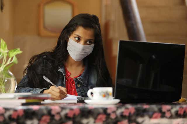 Young woman in face mask studying with computer screen and 