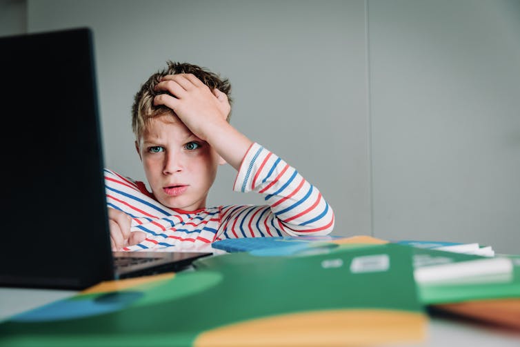 Boy looks at computer screen with hand in hair, thinking.