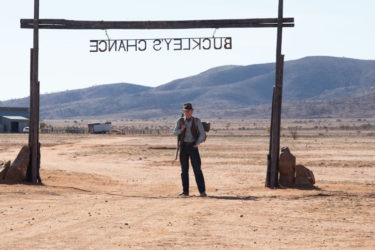 Bill Nighy under a sign, reading Buckley's Chance backwards.