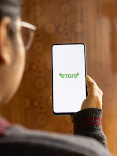 Picture of man holding phone with eToro loading up
