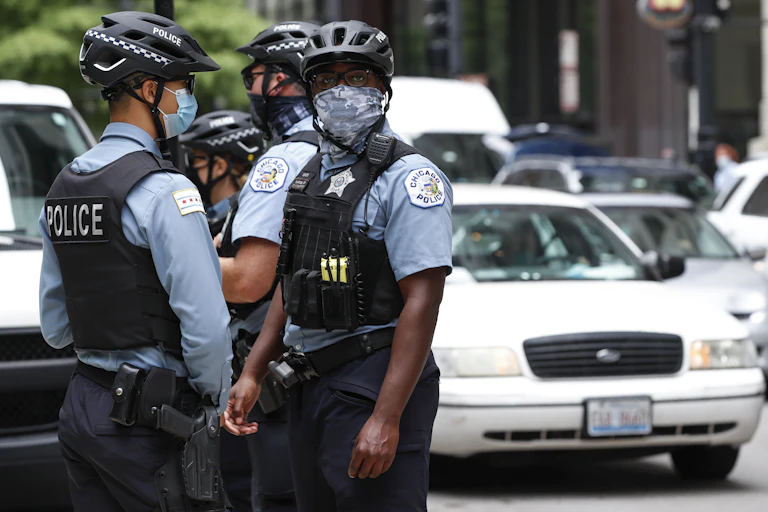 Four Chicago police officers in hard bike helmets and tactical vests standing outside during a protest.