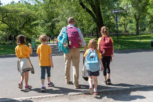 A man walks through a park with four children.