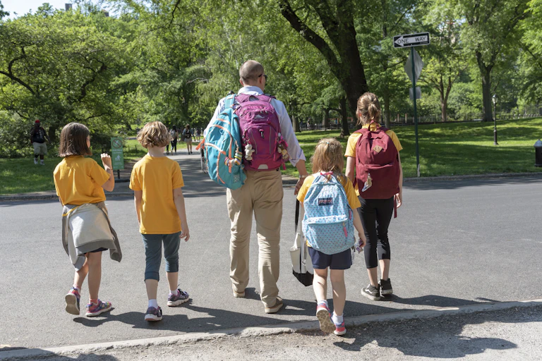A man walks through a park with four children.