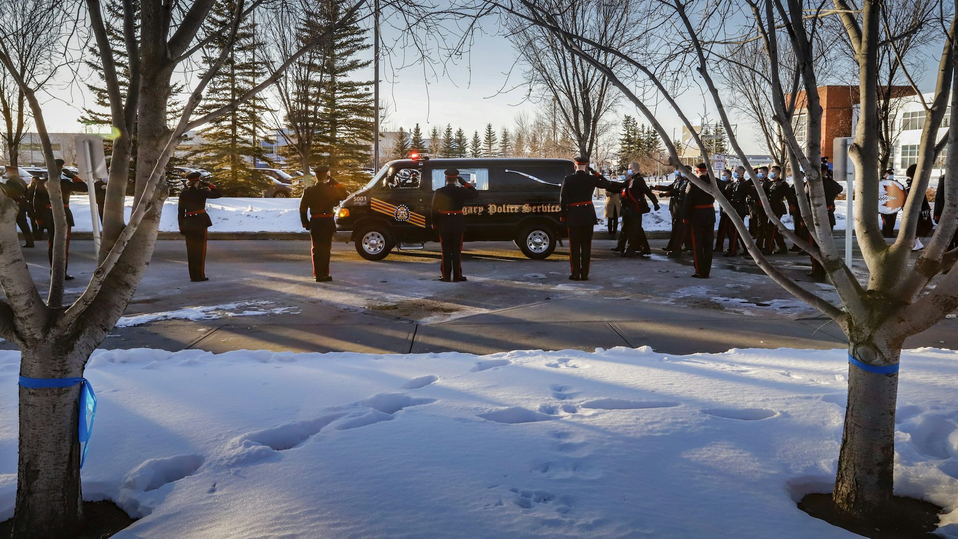 Snow covers the ground as a hearse drives past cops saluting