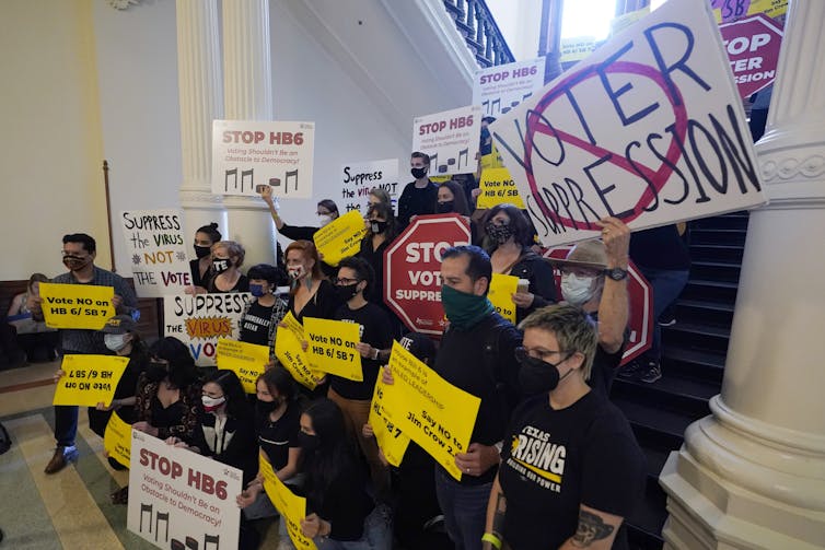 A group carrying signs protesting new voting laws on steps inside the Texas Capitol building.