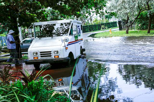 A postal truck parked at the edge of a flooded street.