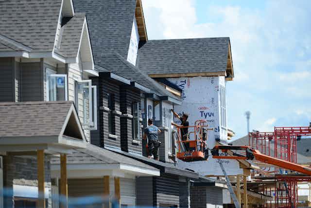 Houses are being built in the suburbs, men are on a cherry picker adding shingles