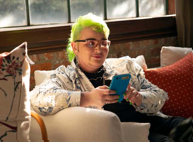 Person with lime green hair sits looking at their phone