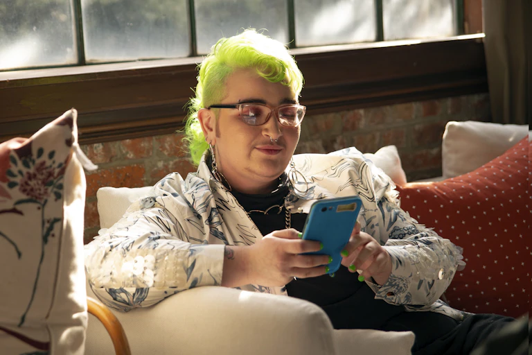 Person with lime green hair sits looking at their phone