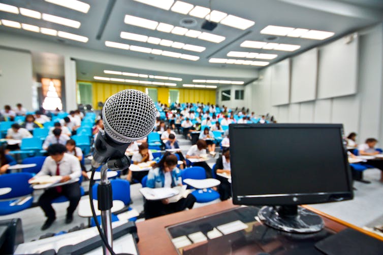 Un écran et un micro disposés sur un bureau devant une classe