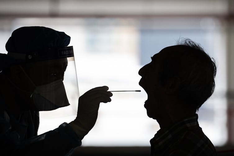 Man in shadow opens mouth to get COVID test.