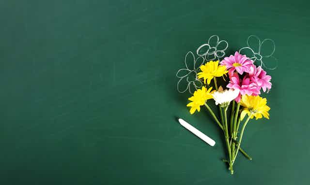A boquet of flowers in front of a chalkboard with chalk flowers drawn behind them.