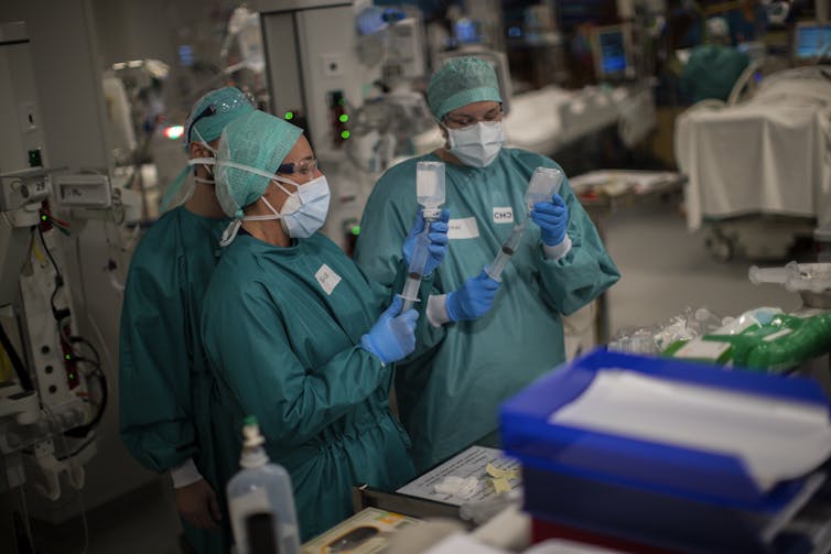 Two health workers in PPE inject fluid into a syringe.