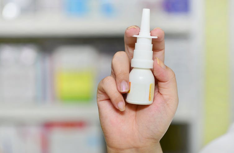 Close up of a person holding a nasal spray in their hand.