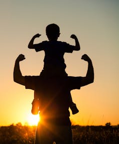 Father with son on his shoulders with both flexing their muscles.