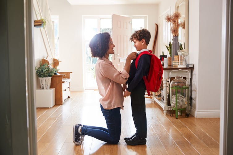 Mum on her tees fixing her son's school tie. He's wearing uniform and backpack.