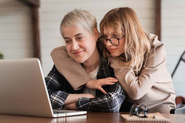 Two women cuddling looking at laptop screen
