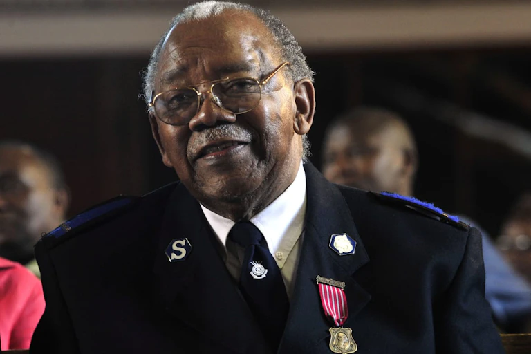 A bespectacled man wearing a jacket with Salvation Army is photographed smiling.
