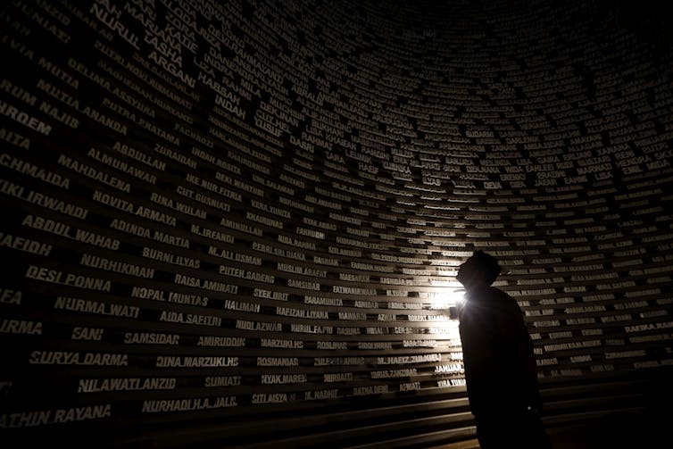 A man gazes at a wall of names in a dark room