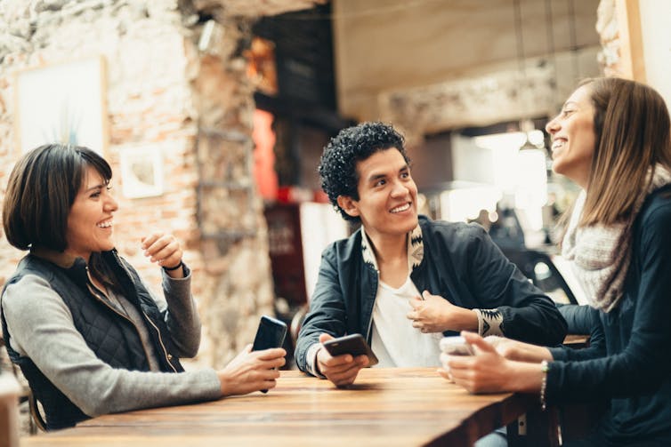 Three people sit at a table and talk