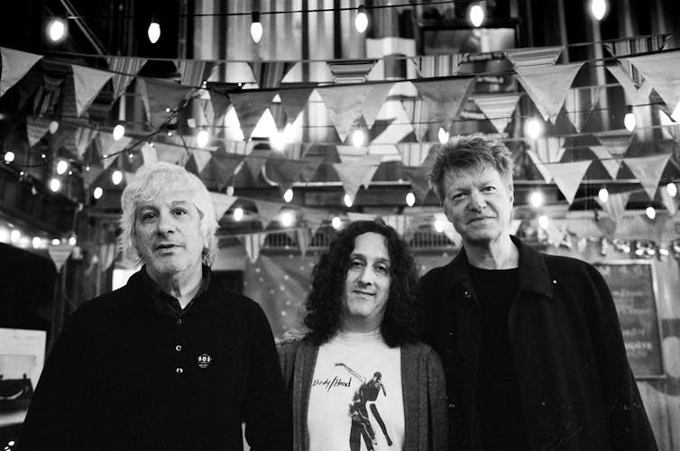 Three men standing next to each other in a line with arms around each other in a black and white photo.