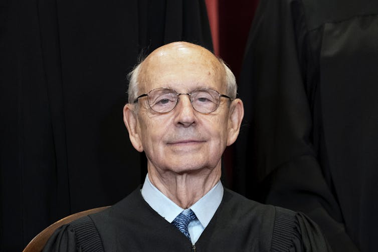 An elderly man with wire-rimmed glasses in a Supreme Court black robe.
