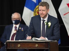 A man standing at a podium in front of the Nova Scotia flag