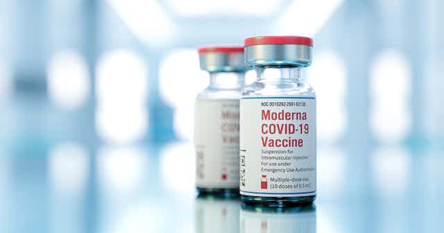 Two vials of Moderna COVID-19 vaccine against blurred background
