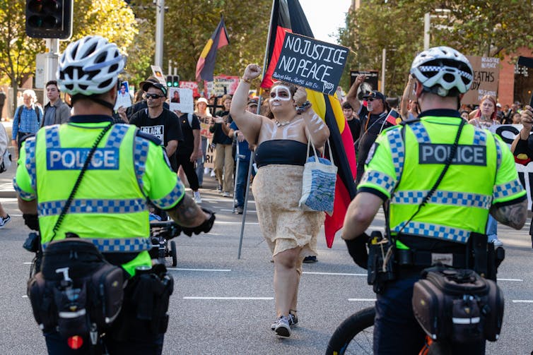 Woman protestor with placard approaches police officers at a rally.