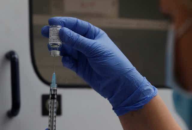 A gloved hand inserts a vial of the Novavax vaccine into a syringe.