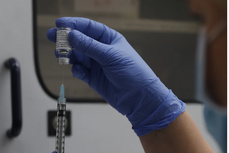 A gloved hand inserts a vial of the Novavax vaccine into a syringe.