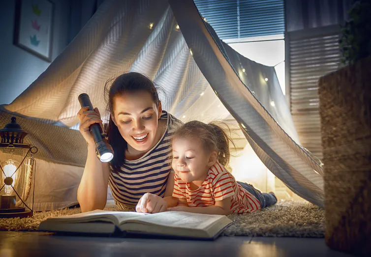 Mum reading book with daughter in a living room tent.
