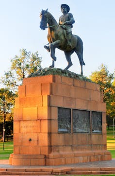 A statue of a man astride a horse, both atop a tan-bricked plinth.