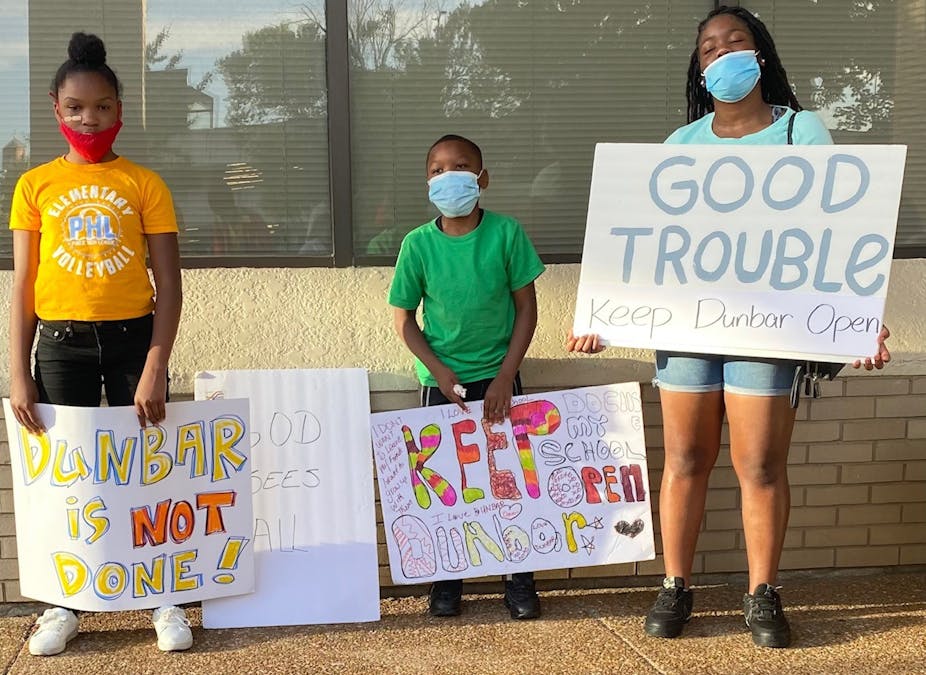 Three kids hold protest signs that read 'Keep Dunbar open'