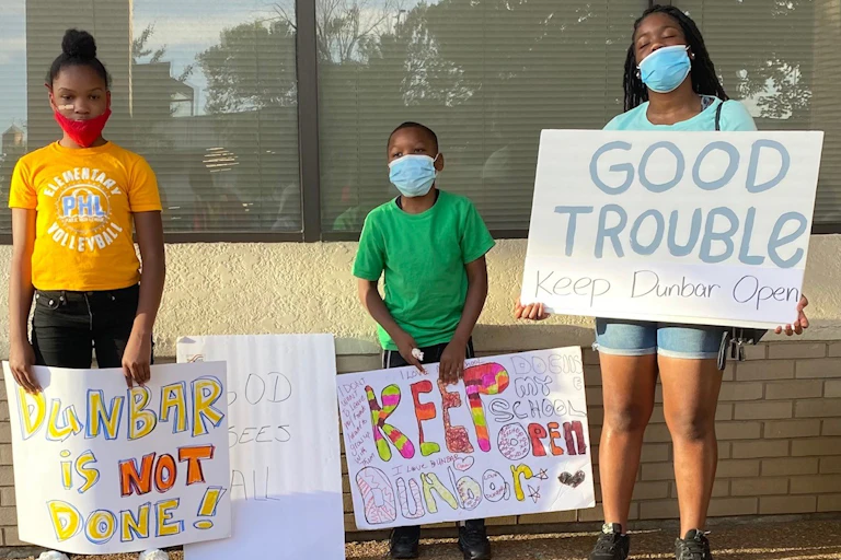 Three kids hold protest signs that read 'Keep Dunbar open'