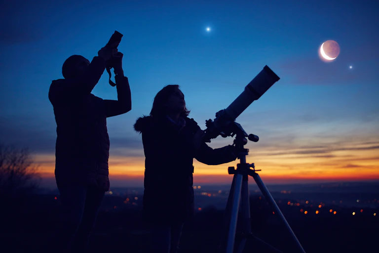 two people silhouettes against a dusk sky, a crescent moon in the background