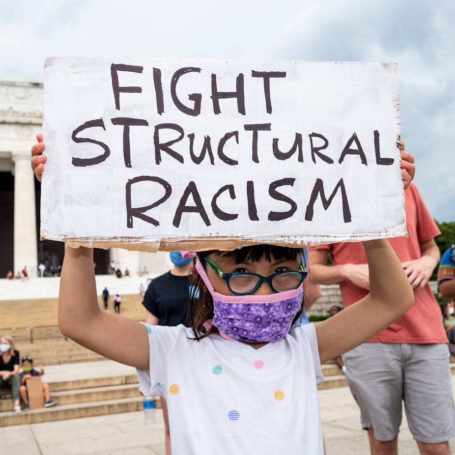 Little girl wearing glasses and a face mask holds up sign that says 'fight structural racism'