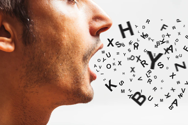A close up, profile-view photo of a man with an assortment of letters appearing to come out of his mouth