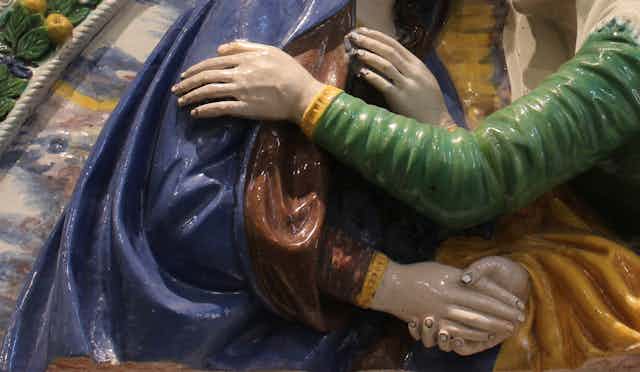 Sculpture showing a hand reaching and resting on a shoulder of a blue-cloaked figure.