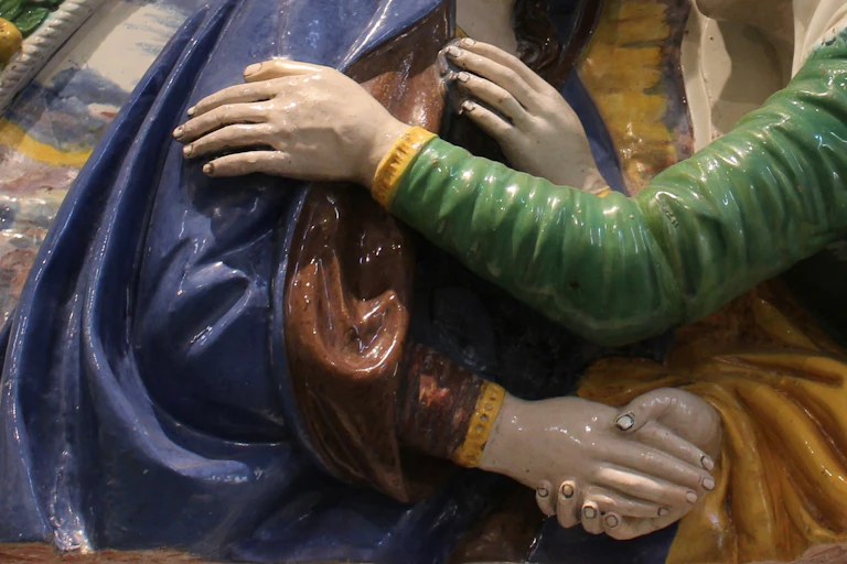 Sculpture showing a hand reaching and resting on a shoulder of a blue-cloaked figure.