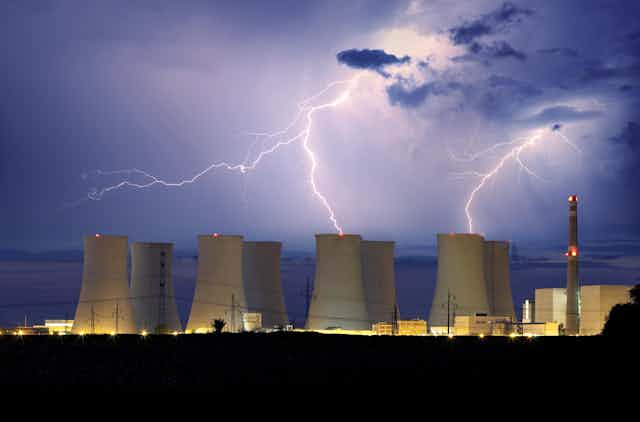 Cooling towers of a nuclear power plant with lightning in the background.