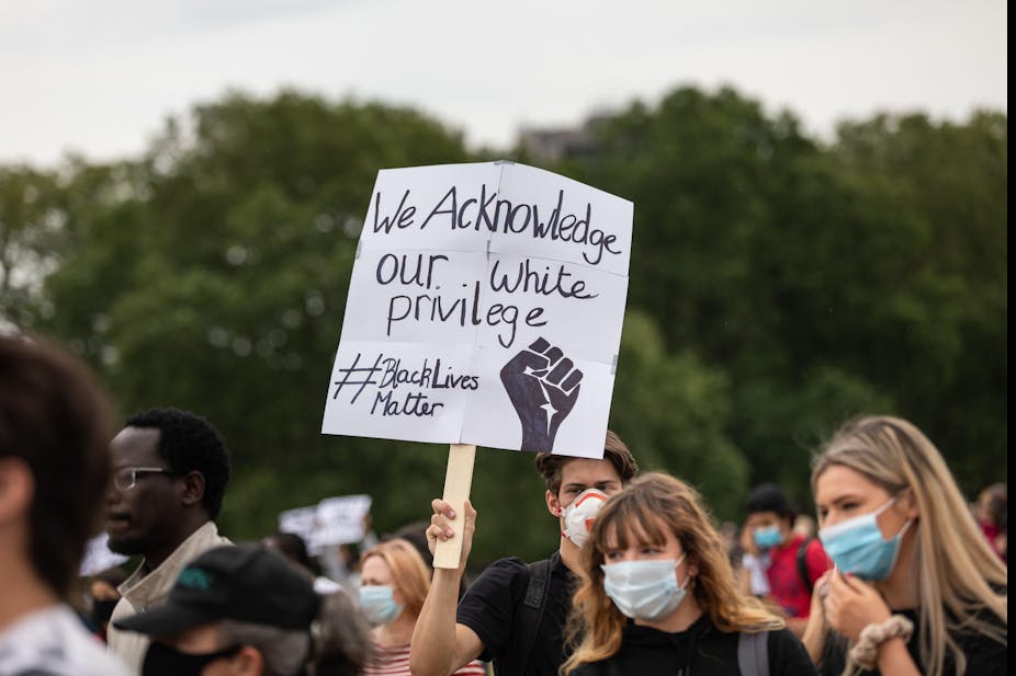 Man holding up sign at Black Lives Matter Protest in London that says 'we acknowledge our white privilege'