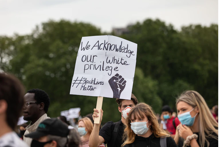 Man holding up sign at Black Lives Matter Protest in London that says 'we acknowledge our white privilege'