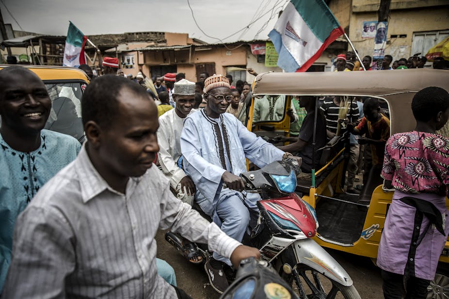 Two men riding a bike get stuck in the traffic created by people celebrating on February 27, 2019 in a street of Kano, the re-election of Muhammadu Buhari as Nigerian president