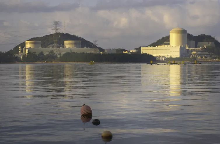 A large nuclear facility on a hill opposite a body of water.