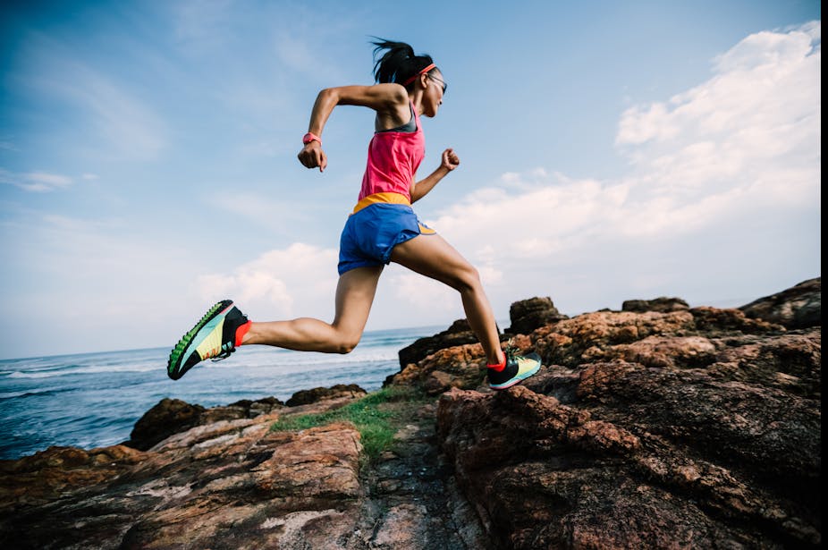 Female trail runner runs up a rocky hill.
