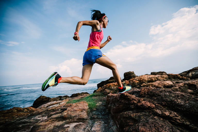 Female trail runner runs up a rocky hill.