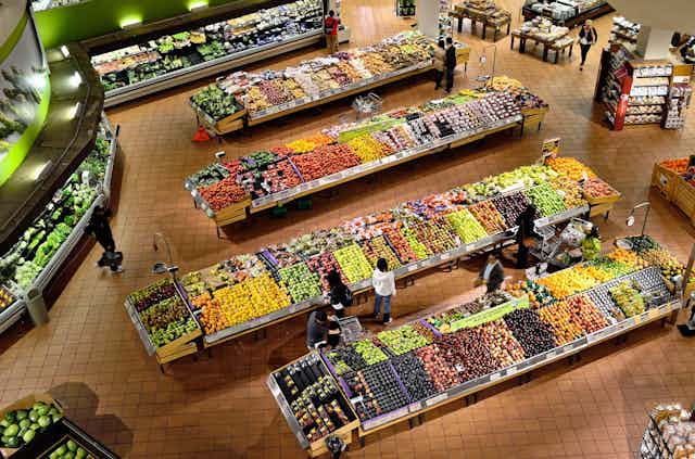 Des gens se promènent dans les allées de fruits et de légumes d'un supermarché. 